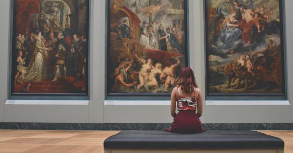 Museum - Woman Sitting on Ottoman in Front of Three Paintings